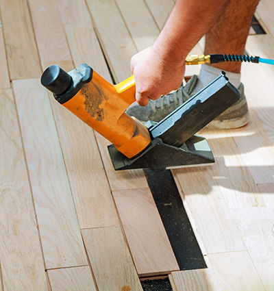 carpenter worker installing wood parquet board during flooring work with hammer