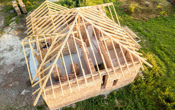 Aerial view of unfinished brick house with wooden roof structure under construction.