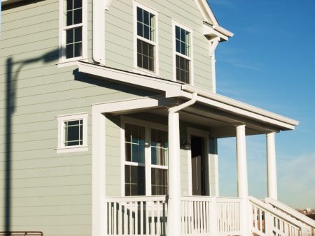 A house with green siding, white railing, and columns.