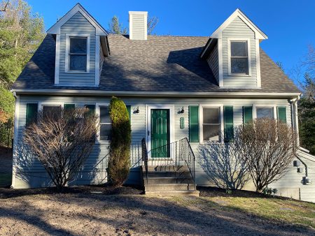 A grey house with green shutters and a small front yard.